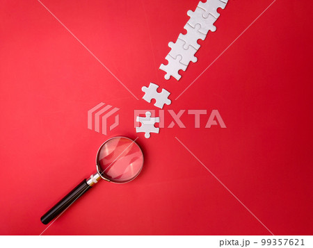 Magnifying glass searching missing puzzle on red background 99357621