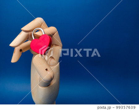 Wooden hand holding love padlock on a blue background. Wooden hand holding love padlock on a blue background. 99357639