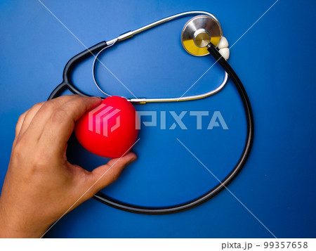 Hand holding red heart with statehoscop on blue background. Healthcare and medical concept. 99357658