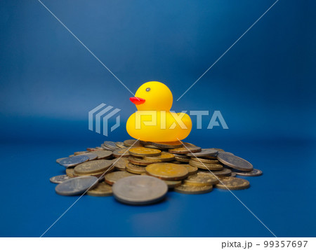 A toy yellow duck is on top of a stack of coins on a blue background. Business concept. 99357697