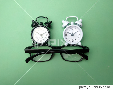 Black and white alarm clock and glasses on a green background. 99357748