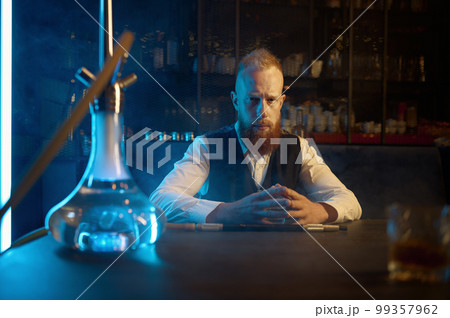 Portrait of lonely bearded man smoking hookah and drinking brandy 99357962