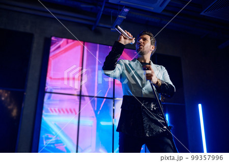 Male singer holding microphone standing and performing on stage Male singer holding microphone standing and performing on stage 99357996