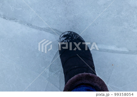 Foot standing on cracked natural lake ice texture. Concept of danger exit to badly frozen water Foot standing on cracked natural lake ice texture. Concept of danger exit to badly frozen water 99358054