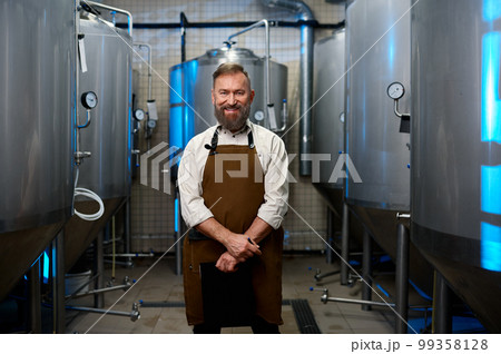 Portrait of smiling brewer man in apron standing among distillery vats Portrait of smiling brewer man in apron standing among distillery vats 99358128
