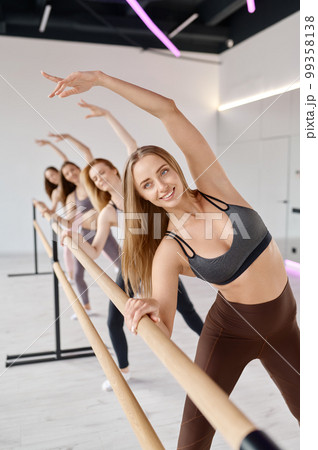 Young women dancers stretching legs, practicing ballet movement at barre 99358138