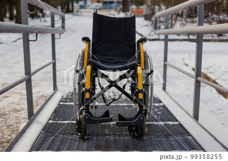 Empty wheelchair in the hospital on the ramp. Wheelchair close-up. Children's wheelchair Empty wheelchair in the hospital on the ramp. Wheelchair close-up. Children's wheelchair 99358255