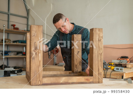 Male carpenter finishing work on wooden table in workshop.  99358430