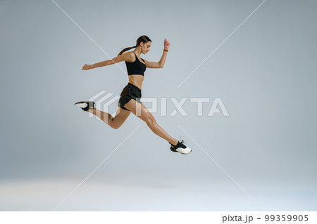 Sporty girl jumping doing split leap in air with joyful expression. Flexible and weightless concept Sporty girl jumping doing split leap in air with joyful expression. Flexible and weightless concept 99359905