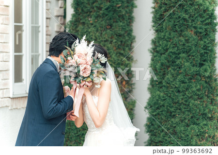 結婚式で結婚式場の庭でブーケを持ちながらキスをする新郎新婦（ガーデンウェディング） 99363692