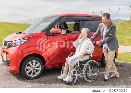 自動車の前にいる車椅子の高齢者女性と男性（シニア・夫婦・男女） 99370235