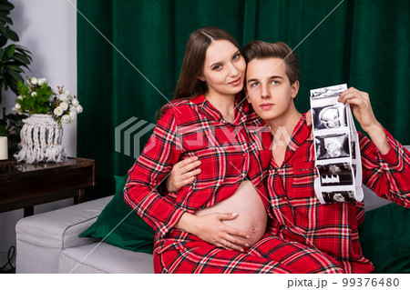 Pregnant woman sitting on the lap of a man holding usg photos Pregnant woman sitting on the lap of a man holding usg photos 99376480