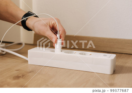Human hand puts the charger into the extension cord. White cable connector Human hand puts the charger into the extension cord. White cable connector 99377687