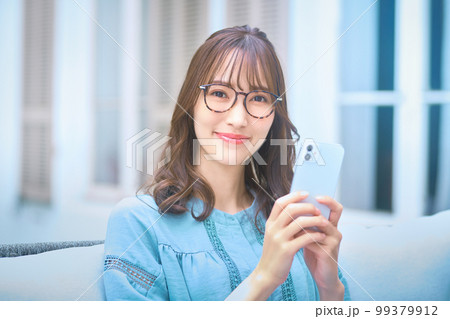 自宅の庭でスマホを操作するメガネをかけた若い女性 99379912