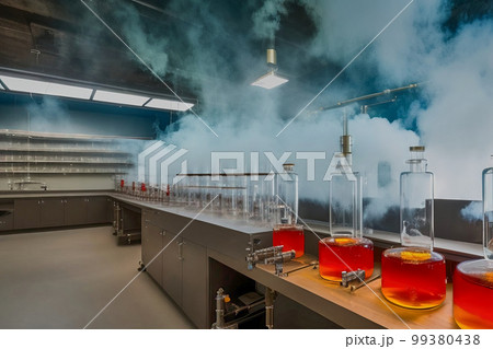 Chemical laboratory with flasks with glowing liquid in the foreground and experiments with heavy fumes at the end of the laboratory table, made with generative AI 99380438