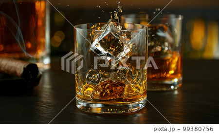 ice cube fall into a glass with whiskey drink. ice cube fall into a glass with whiskey drink. 99380756