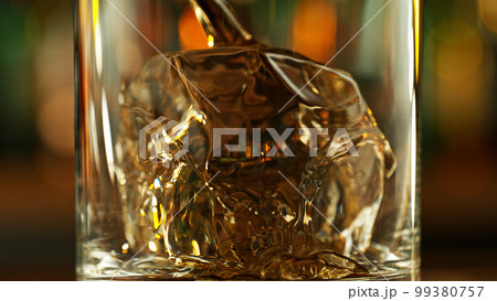 Detail of pouring whiskey into glass with ice cubes. Detail of pouring whiskey into glass with ice cubes. 99380757