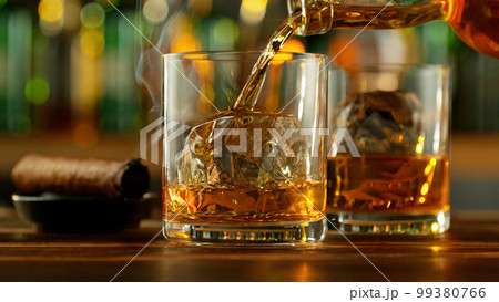Detail of pouring whiskey into glass with ice cubes. 99380766