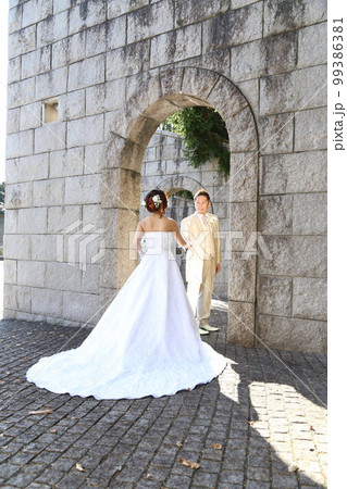石のアーチの前でウエディングドレスとタキシード姿の新郎新婦ロケ撮影 99386381
