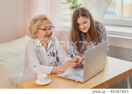 Adult granddaughter teaching her elderly grandmother to use laptop 99387663