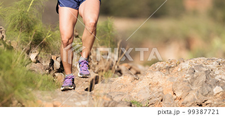 Trail running athlete exercising for fitness and health outdoors on mountain pathway, closeup of running shoes in action 99387721
