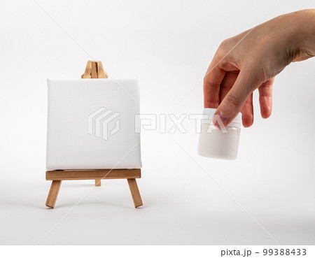 Canvas mockup on wood mini tiny easel, artists hand with blank jar of gouache paint. Minimali creative tools, drawing supplies Canvas mockup on wood mini tiny easel, artists hand with blank jar of gouache paint. Minimali creative tools, drawing supplies 99388433
