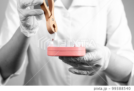 Dentist pulling tooth with forceps out of jaw model. Teeth extraction, loosing, stomatology concept. Work of dental surgeon in lab coat and gloves. 99388540
