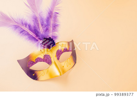 Happy Purim carnival decoration. Top view venetian ball mask with purple feather on pastel background, Jewish Purim and Mardi Gras in Hebrew, holiday background banner design, Masquerade party Happy Purim carnival decoration. Top view venetian ball mask with purple feather on pastel background, Jewish Purim and Mardi Gras in Hebrew, holiday background banner design, Masquerade party 99389377