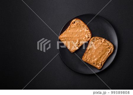 Nutritious sandwich consisting of bread and peanut butter on a black ceramic plate 99389808