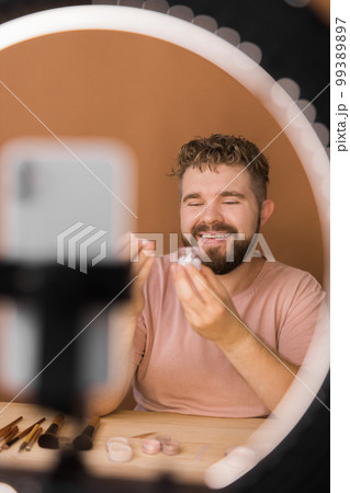 Man talking on cosmetics holding a makeup tools while recording his video. Guy making video for his blog on cosmetic product Man talking on cosmetics holding a makeup tools while recording his video. Guy making video for his blog on cosmetic product 99389897