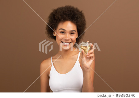 Smiling young black curly lady with perfect skin hold bottle of perfume, recommends ad and offer Smiling young black curly lady with perfect skin hold bottle of perfume, recommends ad and offer 99390240