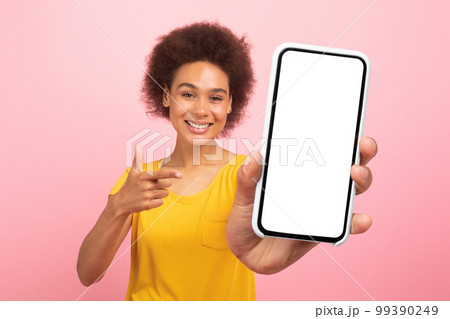 Happy glad pretty young black curly lady pointing finger at smartphone with empty screen 99390249