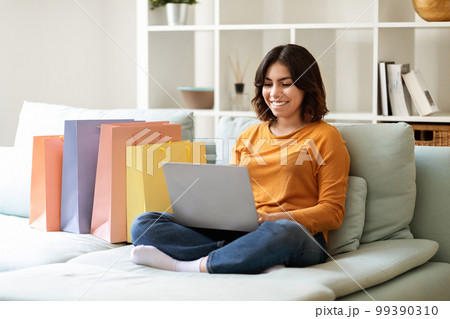 Smiling Young Arab Woman Shopping Online With Laptop At Home Smiling Young Arab Woman Shopping Online With Laptop At Home 99390310