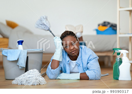 Lazy black woman lying on floor with duster, touching head 99390317