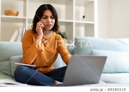 Young Arab Female Working With Laptop And Talking On Cellphone At Home 99390319