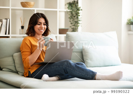 Domestic Pastime. Happy Arab Female Relaxing With Laptop And Coffee At Home 99390322