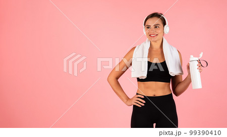 Sporty Lifestyle Concept. Happy young woman in wireless headphones holding fitness bottle Sporty Lifestyle Concept. Happy young woman in wireless headphones holding fitness bottle 99390410