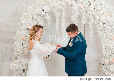 happy bride and groom exchange rings in an arch of artificial flowers. happy bride and groom exchange rings in an arch of artificial flowers. 99391286