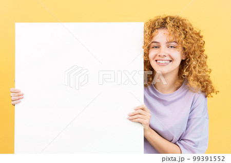 Smiley woman with curly hair holding a blank panel Smiley woman with curly hair holding a blank panel 99391552