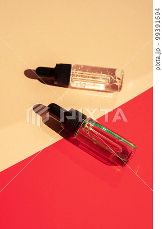 Two glass bottles with cosmetic liquid on bright red background with shadows and light reflections. Two glass bottles with cosmetic liquid on bright red background with shadows and light reflections. 99391694