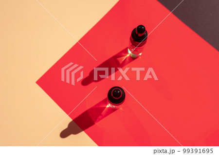 Two glass bottles with cosmetic liquid on bright red background with shadows and light reflections. Two glass bottles with cosmetic liquid on bright red background with shadows and light reflections. 99391695