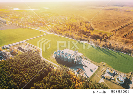 Aerial view modern granary, grain-drying complex, commercial grain or seed silos in sunny autumn rural countryside landscape. Corn dryer silos, inland grain terminal, grain elevators standing in a Aerial view modern granary, grain-drying complex, commercial grain or seed silos in sunny autumn rural countryside landscape. Corn dryer silos, inland grain terminal, grain elevators standing in a 99392005