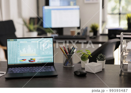 Investment advisory company displaying world stock market data on portable computer screen. Laptop with statistical graphs with unmanned workstations, coworking workplace. 99393487
