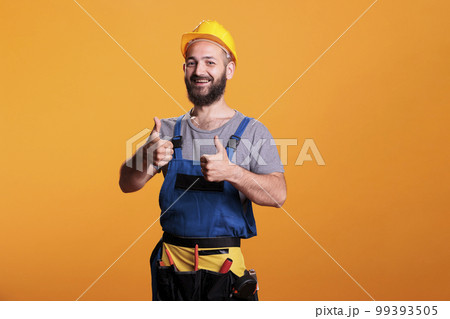 Successful repairman giving thumbs up on camera, showing like and approval gesture in studio. Male construction worker expressing agreement and good symbol, confident happy expert. Successful repairman giving thumbs up on camera, showing like and approval gesture in studio. Male construction worker expressing agreement and good symbol, confident happy expert. 99393505