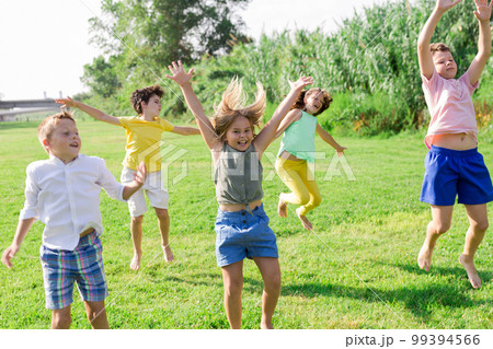Cheerful preteen girls and boys jumping in summer city park 99394566