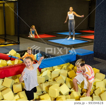 Preteen girl and boy floundering in pit with foam cubes 99394628