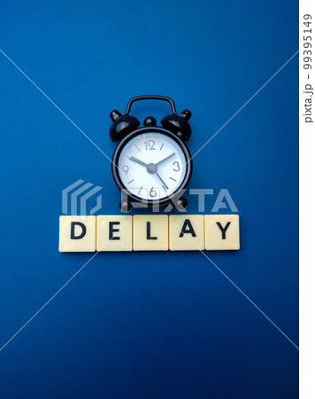 Black alarm clock with the word DELAY on blue background. Black alarm clock with the word DELAY on blue background. 99395149