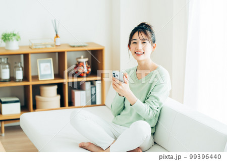 リビングでスマホを見る若い女性 99396440