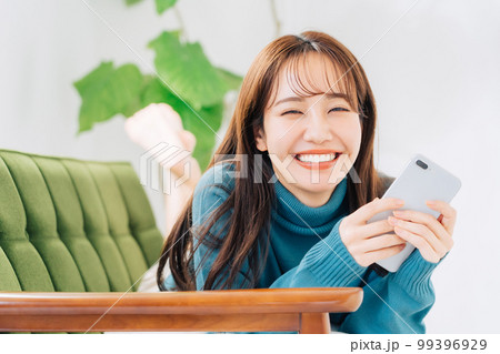 ソファに寝転がってスマホを使う女性 99396929