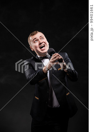 Portrait of emotional young man singing in microphone on black background, singer, actor, leading  99401661
